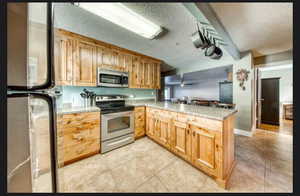 Kitchen featuring appliances with stainless steel finishes, light tile patterned floors, light stone counters, kitchen peninsula, and a textured ceiling