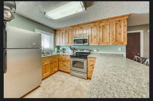 Kitchen with stainless steel appliances, light tile patterned flooring, a textured ceiling, and kitchen peninsula