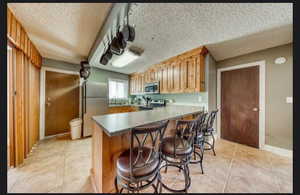 Kitchen with light tile patterned floors, sink, stainless steel appliances, a kitchen bar, and kitchen peninsula