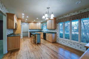 Kitchen with pendant lighting, a kitchen bar, a center island, black appliances, and light wood-type flooring