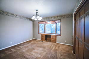 Unfurnished bedroom featuring a notable chandelier, built in desk, a textured ceiling, and carpet