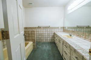 Bathroom featuring vanity, tile walls, and a tub to relax in