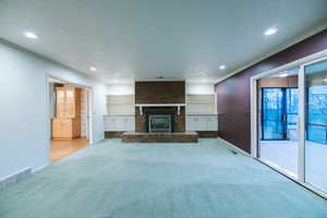 Unfurnished living room featuring built in shelves, crown molding, light carpet, a textured ceiling, and a fireplace