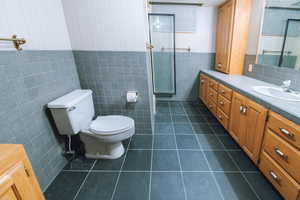 Bathroom featuring tile patterned flooring, vanity, toilet, and tile walls