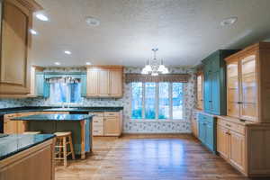 Kitchen with a breakfast bar area, light hardwood / wood-style flooring, dark stone countertops, hanging light fixtures, and a center island