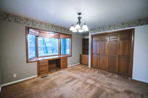 Unfurnished office featuring a notable chandelier, built in desk, light colored carpet, and a textured ceiling