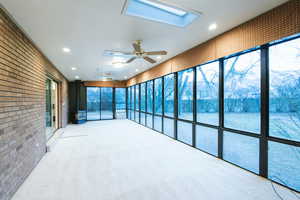 Unfurnished sunroom with ceiling fan and a skylight