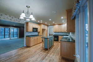 Kitchen featuring pendant lighting, sink, light hardwood / wood-style flooring, black appliances, and a kitchen island