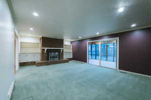 Unfurnished living room featuring light carpet, built in features, and a textured ceiling