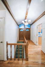 Foyer entrance with hardwood / wood-style flooring, lofted ceiling with beams, and a notable chandelier