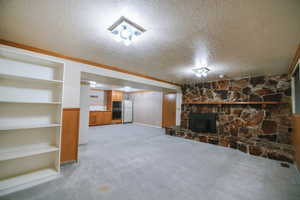 Unfurnished living room featuring built in features, a fireplace, ornamental molding, a textured ceiling, and light carpet