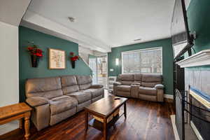 Living room featuring dark wood-type flooring, a textured ceiling, and a fireplace