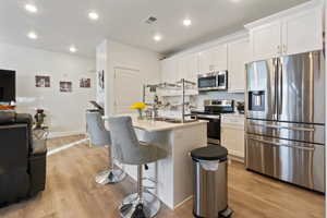 Kitchen featuring stainless steel appliances, sink, an island with sink, and white cabinets