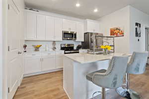 Kitchen featuring an island with sink, white cabinets, a kitchen breakfast bar, stainless steel appliances, and light hardwood / wood-style flooring