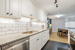 Kitchen featuring sink, white cabinetry, stainless steel appliances, light stone counters, and tasteful backsplash