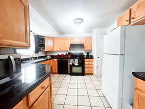 Kitchen with sink, light tile patterned floors, a textured ceiling, and black appliances