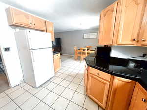 Kitchen featuring white fridge, light tile patterned floors, and light brown cabinets