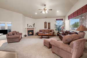 Carpeted living room featuring ceiling fan, high vaulted ceiling, and a fireplace