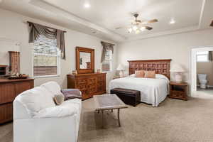 Bedroom with ceiling fan, ensuite bath, a tray ceiling, and carpet