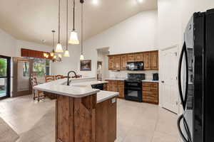 Kitchen with a breakfast bar, sink, hanging light fixtures, black appliances, and a center island with sink