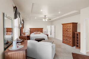 Carpeted bedroom featuring a raised ceiling and ceiling fan