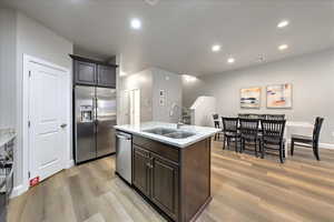 Kitchen featuring sink, light wood-type flooring, stainless steel appliances, light stone countertops, and a kitchen island with sink