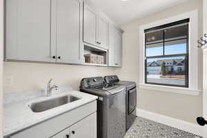 Laundry area with cabinets, separate washer and dryer, sink and decorative tile flooring.