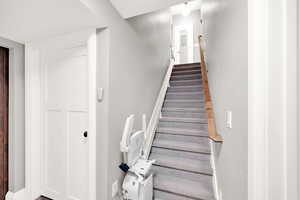 View of stairs to basement with automatic chair rail. The door goes to an unfinished storage space and utility closet.