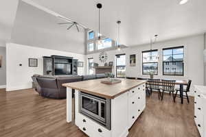 Kitchen featuring composite hardwood LVP flooring, decorative light fixtures, a center island with storage, stainless steel microwave, and white cabinets. Here you can see the open plan dining and adjoining living room.