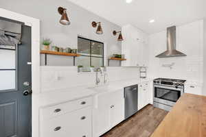 Kitchen featuring white cabinets, appliances with stainless steel finishes, sink, and wall chimney range hood, additional faucet and subway tile.