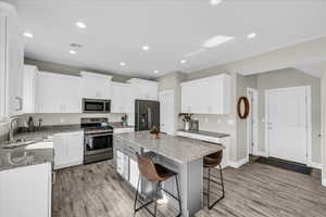 Kitchen featuring white cabinetry, sink, a center island, stainless steel appliances, and light stone countertops