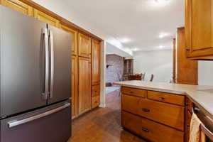 Kitchen featuring dark hardwood / wood-style flooring, brick wall, stainless steel fridge, and kitchen peninsula