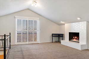 Unfurnished living room featuring a large fireplace, lofted ceiling, carpet, and a textured ceiling