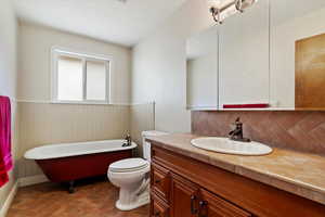 Bathroom featuring a tub to relax in, vanity, toilet, and backsplash