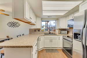 Kitchen with a breakfast bar, sink, white cabinetry, appliances with stainless steel finishes, and kitchen peninsula