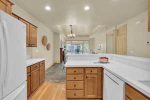 Kitchen featuring pendant lighting, a notable chandelier, a raised ceiling, white appliances, and light hardwood / wood-style flooring