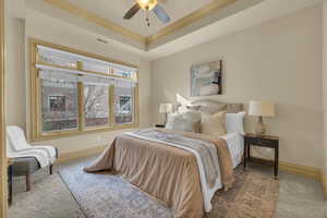 Bedroom with a tray ceiling, ornamental molding, ceiling fan, and carpet flooring