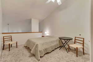 Carpeted bedroom featuring ceiling fan and vaulted ceiling