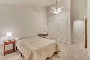 Bedroom featuring high vaulted ceiling, light colored carpet, multiple closets, and ceiling fan