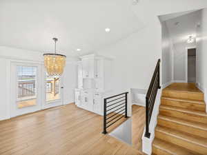 Staircase with wood-type flooring, vaulted ceiling, and a notable chandelier