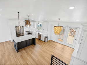 Kitchen featuring appliances with stainless steel finishes, white cabinetry, hanging light fixtures, a center island, and light wood-type flooring