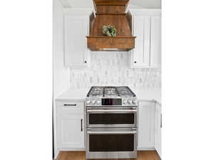 Kitchen with white cabinetry, double oven range, and custom exhaust hood