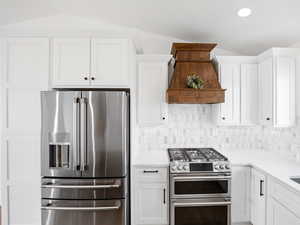 Kitchen featuring premium range hood, white cabinetry, high quality appliances, and lofted ceiling