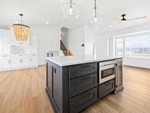 Kitchen with pendant lighting, stainless steel microwave, white cabinets, a center island, and light hardwood / wood-style floors