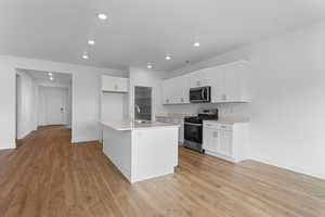 Kitchen featuring appliances with stainless steel finishes, sink, a center island with sink, and white cabinets