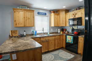 Kitchen featuring dark wood-type flooring, kitchen peninsula, sink, and black appliances