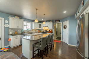 Kitchen with white cabinetry, hanging light fixtures, a center island, and appliances with stainless steel finishes