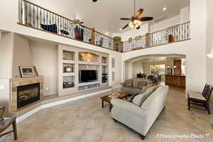 Tiled living room with a towering ceiling, a fireplace, built in features, and ceiling fan