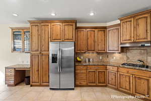 Kitchen featuring backsplash, light tile patterned flooring, stainless steel appliances, and stone countertops