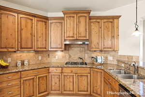 Kitchen with sink, light stone counters, decorative light fixtures, stainless steel appliances, and decorative backsplash